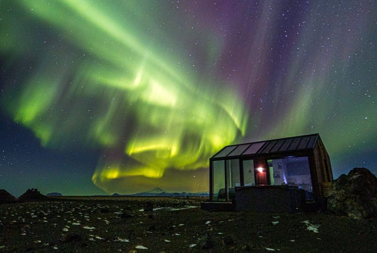 glass-cottage-northern-lights-iceland-airbnb-my-modern-met-1 Glass Cottages Iceland — a luxury glass cabin with panoramic views of moss-covered lava fields beneath the Northern Lights.