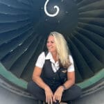 Image of flight attendant, Sherry Martin Peters, sitting inside of an airplane engine. The blog is about learning to pack like a flight attendant. And details about her work being featured in the press.